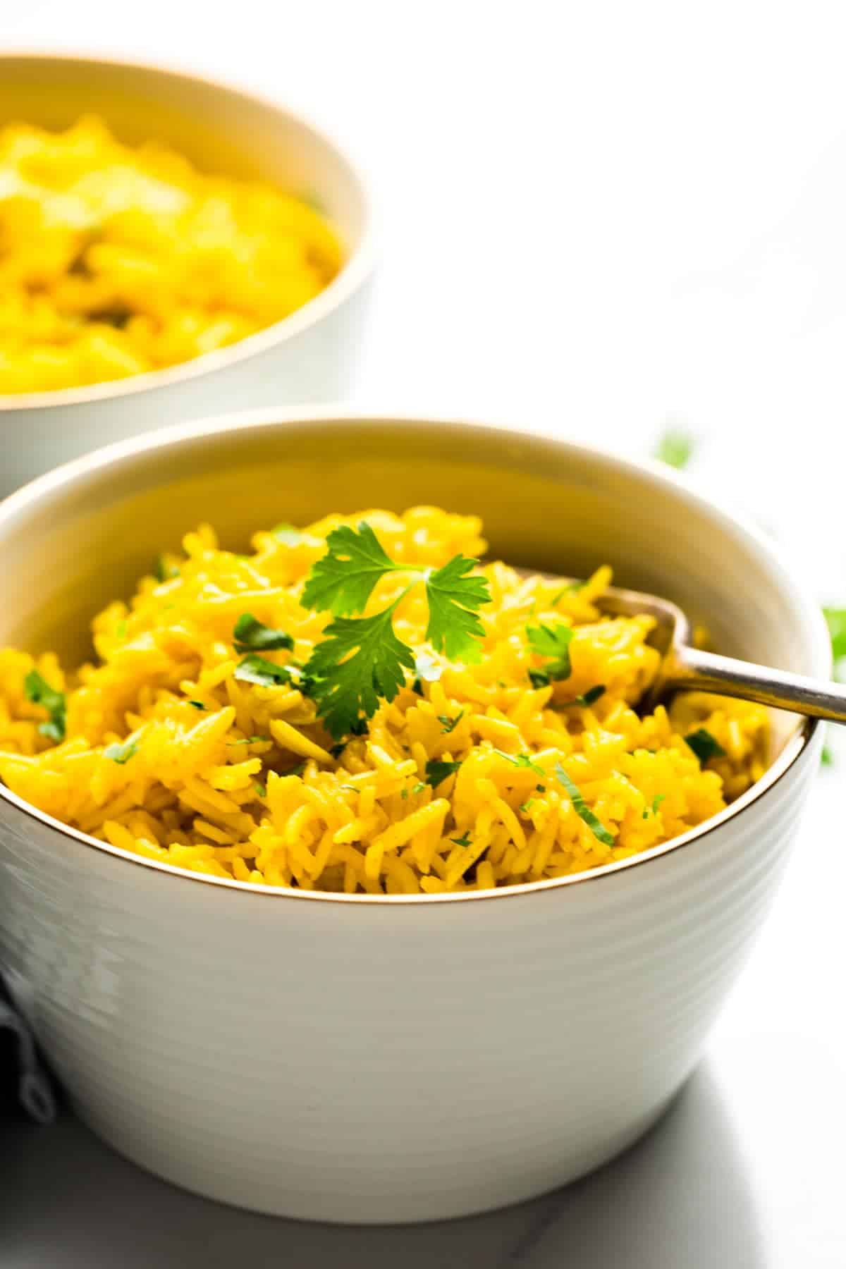 Side view of turmeric rice in a white bowl with parsley leaves as a garnish