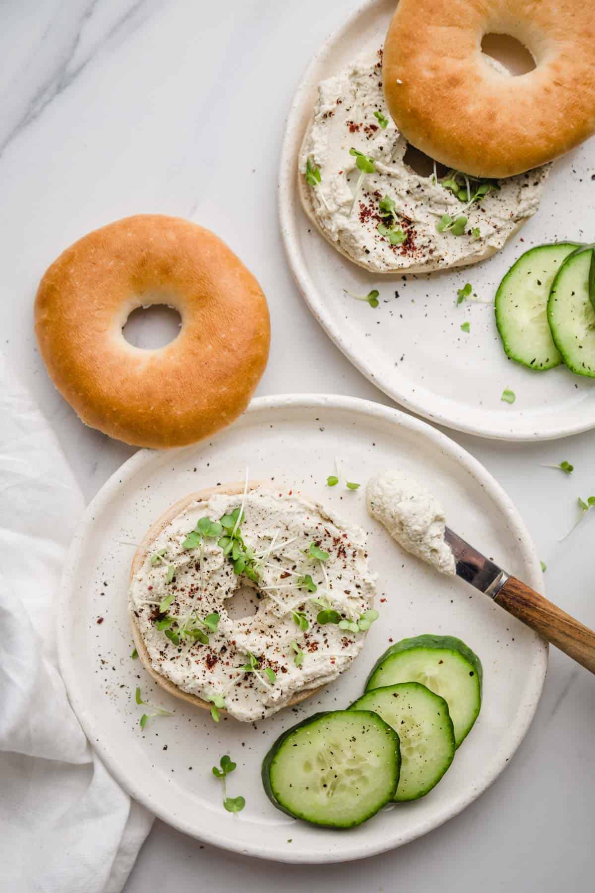 2 plates with sliced bagels and cream cheese, cucumber slices and water cress