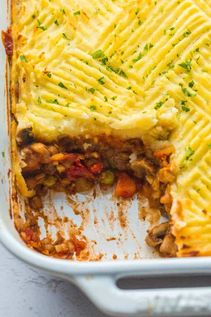 Overhead closeup picture of shepherds pie showing one scoop removed to expose the vegetable stew beneath.
