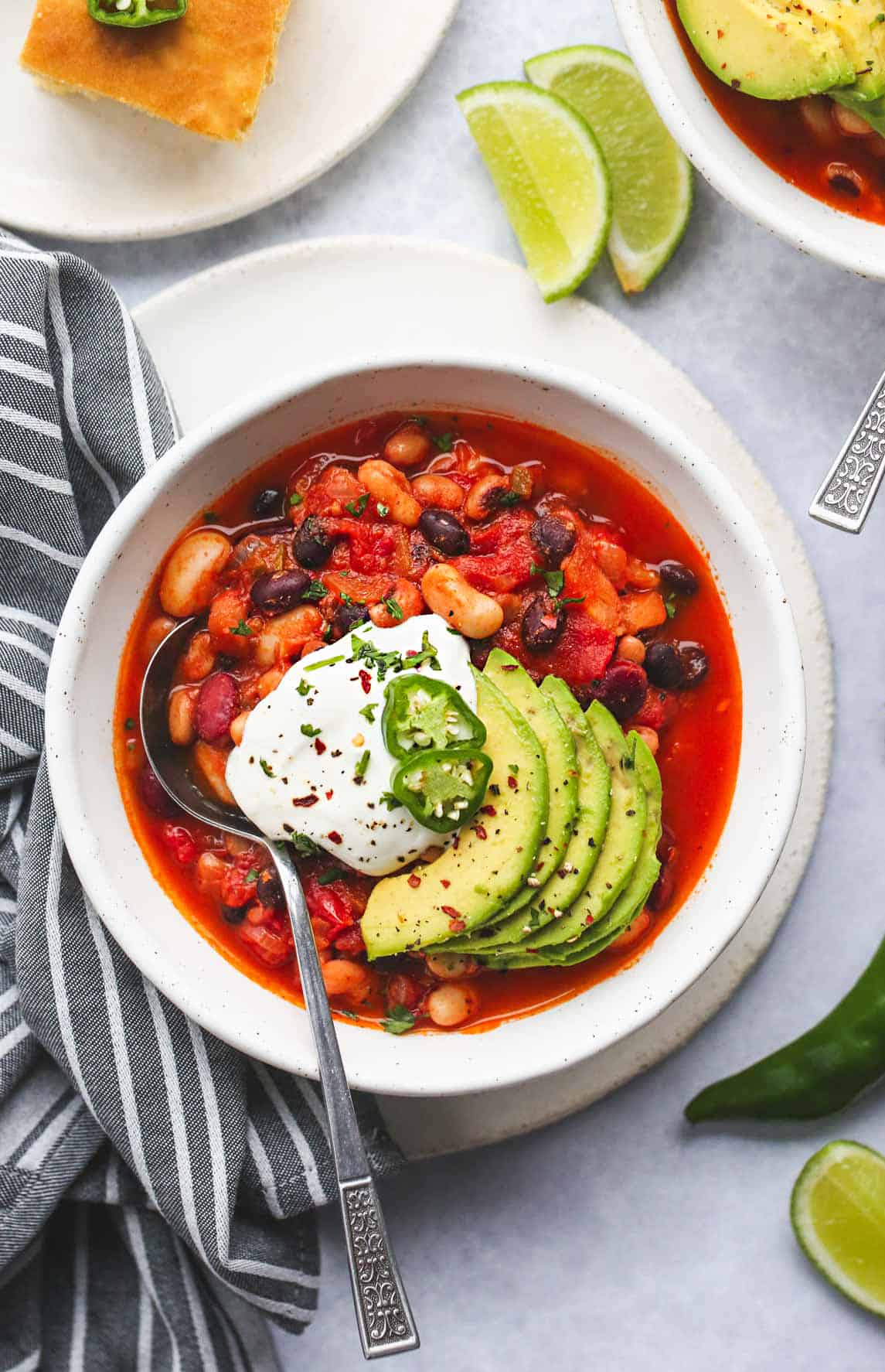 Vegan chili in a white bowl, topped with avocado, vegan sour cream, and jalapeño slices. Overhead shot.