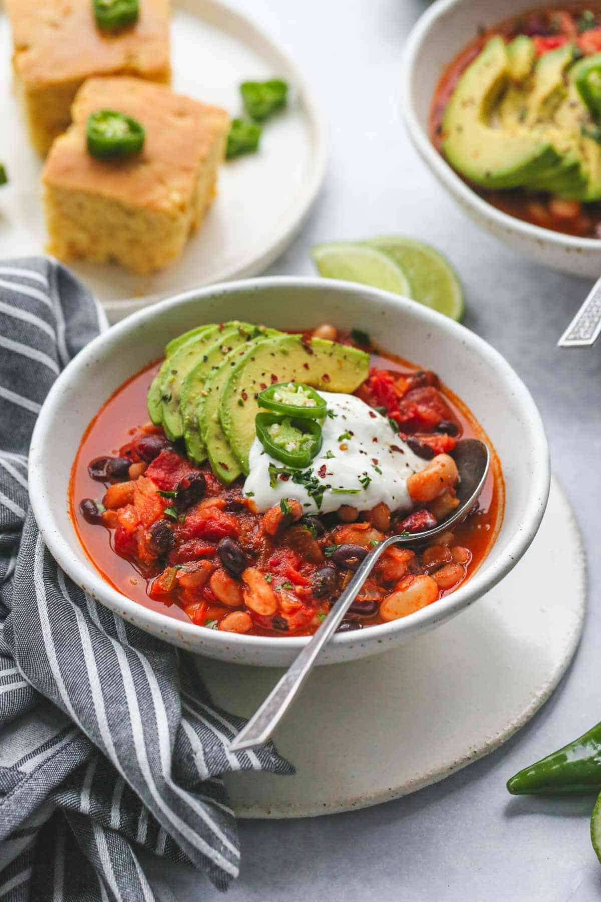 Vegan chili in a white bowl, topped with avocado, vegan sour cream, and jalapeño slices.