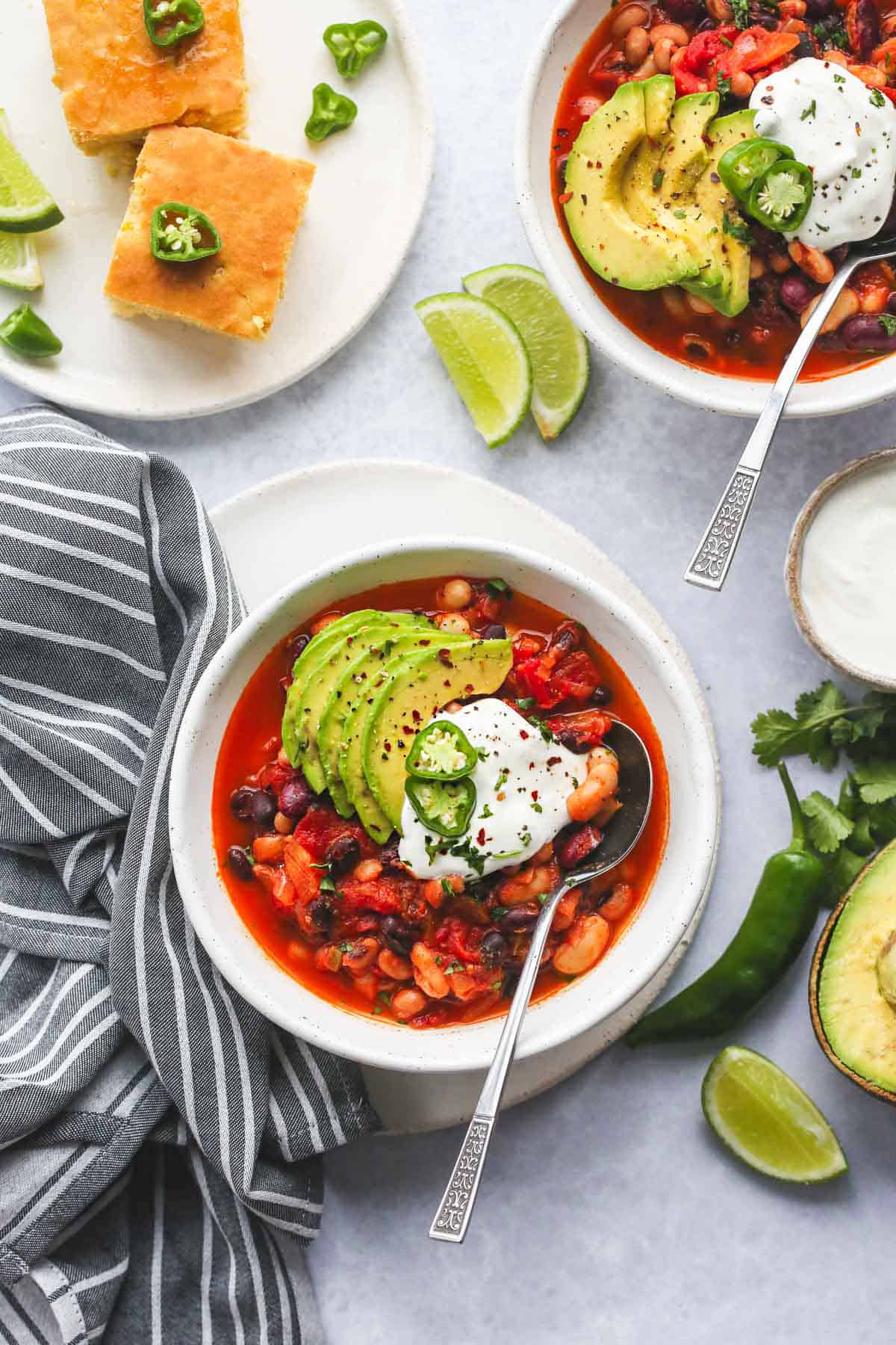 A vegan chili dinner served in 2 white bowls, with sour cream, lime, jalapeños. 